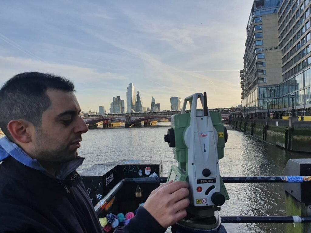 Surveyor using Leica total station conducting measured building survey near River Thames in London