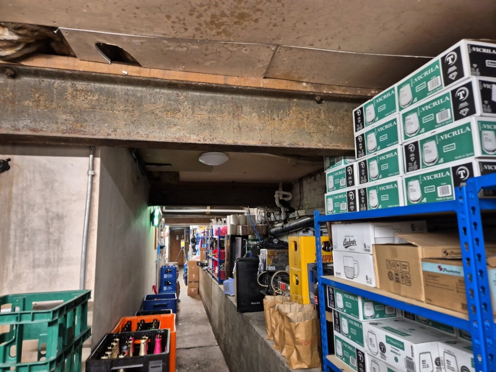 Narrow cellar corridor with keg and glassware storage during building survey